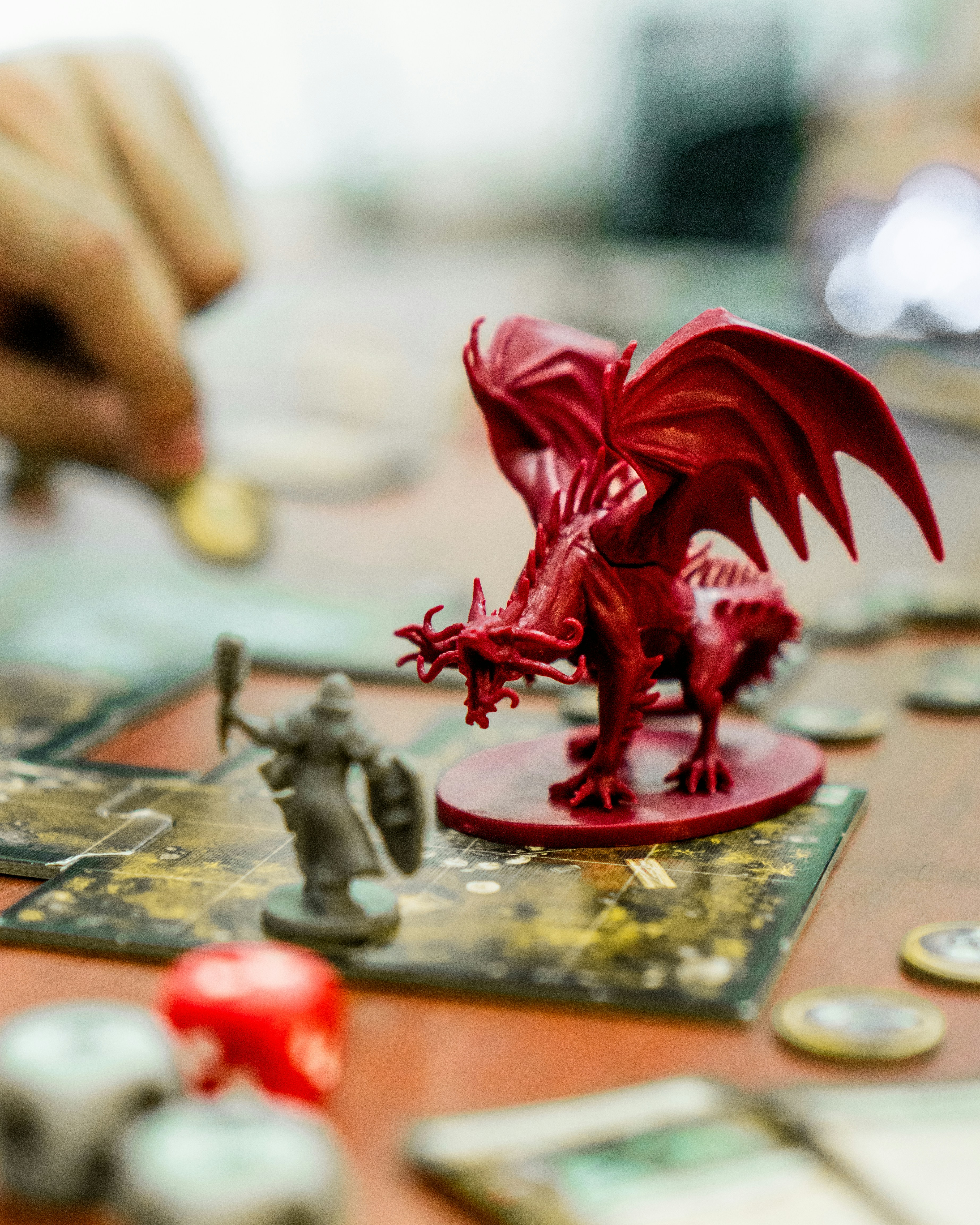 El tablero de un juego de rol sobre el que hay una figura de un guerrero y un dragón, de fondo aparecen las manos de los jugadores.